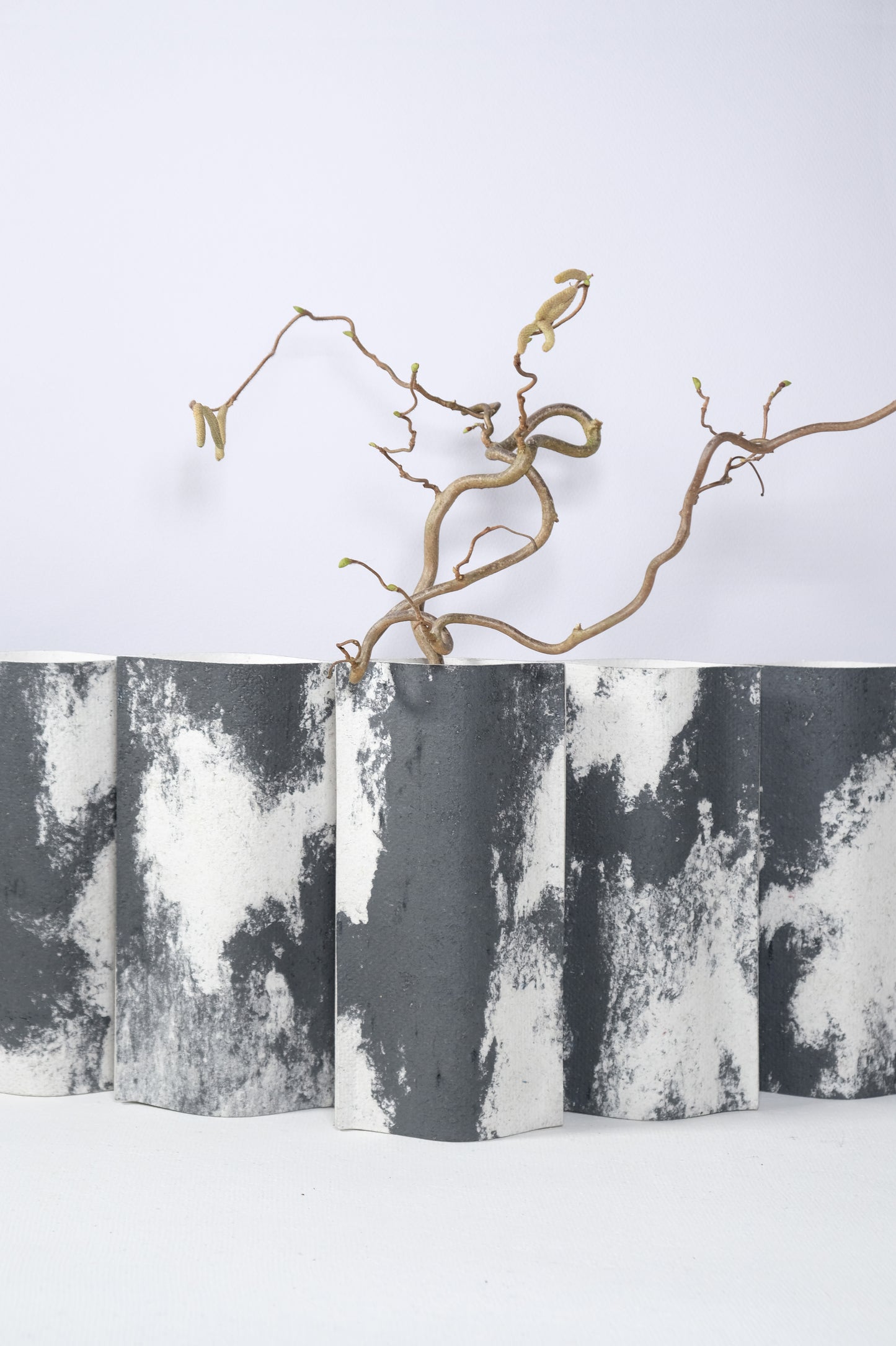 Ensemble de vases de la série ébène de profil rectangulaire sur fond blanc. Ces vases sont fabriqués à partir de deux feuilles de carton-pierre collées à leurs extrémités et ouvertes en leur centre pour y laisser passer un contenant étanche. Les vases arborent un effet marbré avec des veines couleur noir sur fond blanc. Chaque vase a un marbré unique.